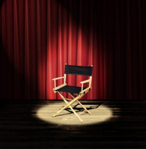 A directors chair on a stage with a red curtain and spotlight